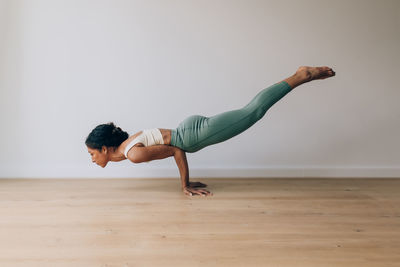 Yoga teacher practicing yoga position of peacock against white wall and wood floor with copy space