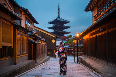 Rear view of mid adult woman standing on street against cloudy sky at dusk