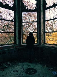 Rear view of woman looking through abandoned house window