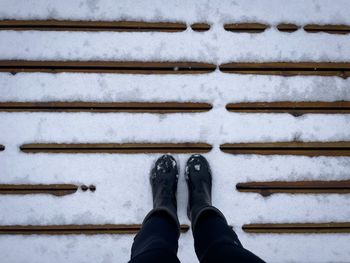 Personal perspective of female black boots standing on a wooden pontoon covered in snow