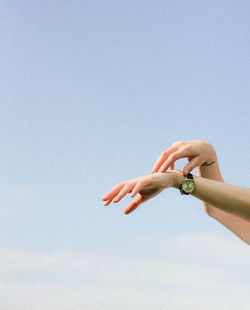 Cropped hands of woman wearing wristwatch against clear sky