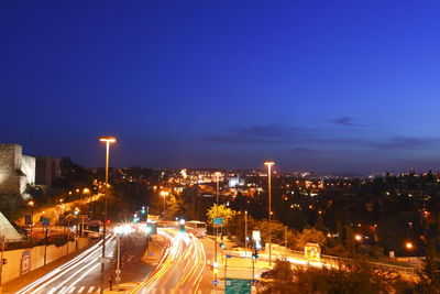 Light trails on road amidst buildings against sky at night