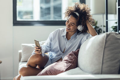 Happy woman using mobile phone sitting on sofa in living room