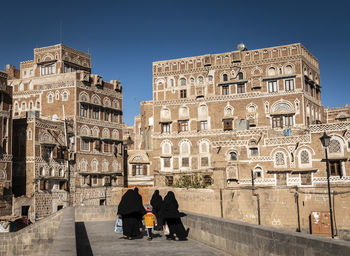 Rear view of people walking on footbridge against buildings in city