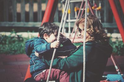 Side view of grandmother with grandson sitting on swing at playground