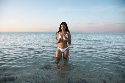 Full length portrait of young woman in sea against sky