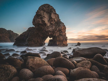 Rocks on beach against sky during sunset