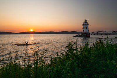 Lighthouse by sea against sky during sunset