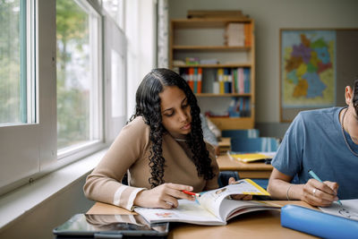 Teenage girl reading book while sitting in classroom