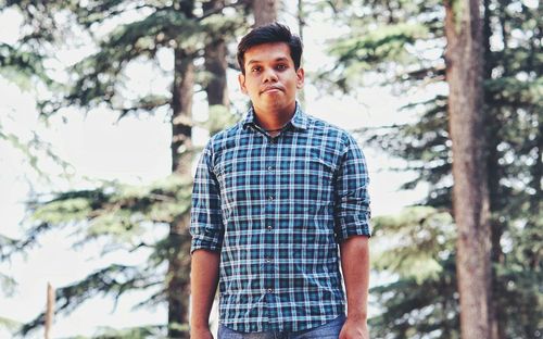 Portrait of young man standing against trees