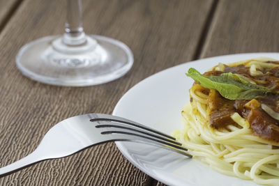 View of spagetti bolognese with green basil. silver fork placed next to the white plate.