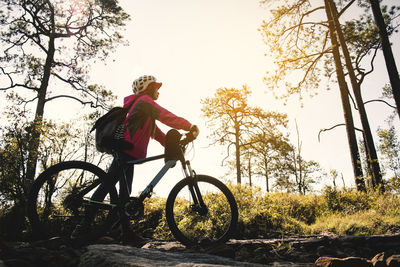 Low angle view of woman with bicycle in forest against sky