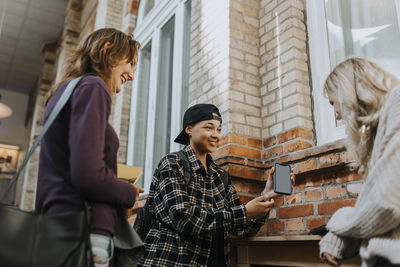 Smiling man showing smart phone to female friends in corridor