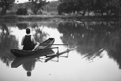 Rear view of man fishing on outrigger over lake