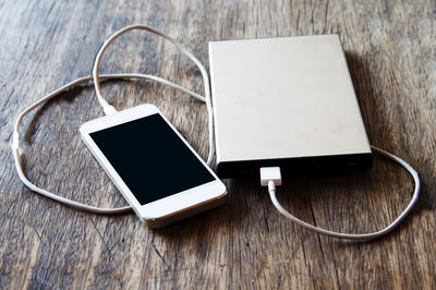 High angle view of mobile phone with powerbank on wooden table