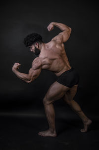 Rear view of shirtless bodybuilder against black background