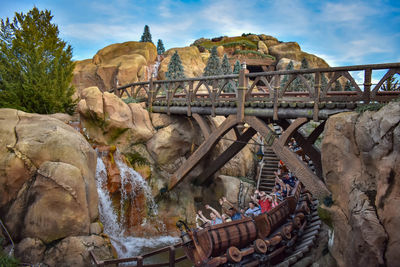 Group of people on rocks by bridge against sky