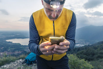 Mature male hiker using smart phone while standing against sky at sunset