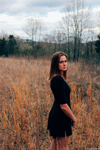 Young woman looking away while standing on field