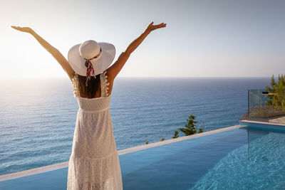 Rear view of woman with arms raised standing against blue sky