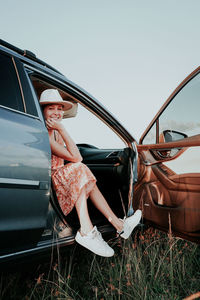 Full length of woman sitting on car against sky