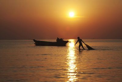 Silhouette fisherman holding fishing net in sea against sky during sunset