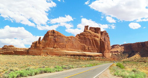 Road leading towards mountain against cloudy sky