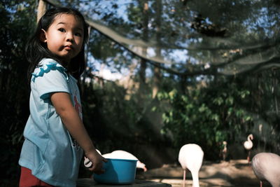 Side view of cute girl looking away while standing against trees