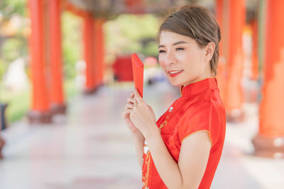 Portrait of smiling woman holding red while standing outdoors