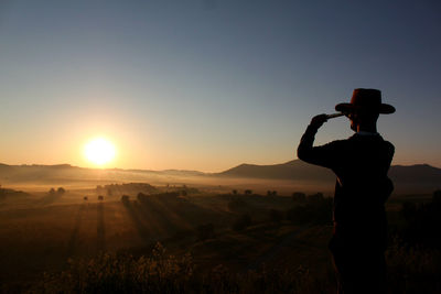 Rear view silhouette man standing on land against sky during sunset