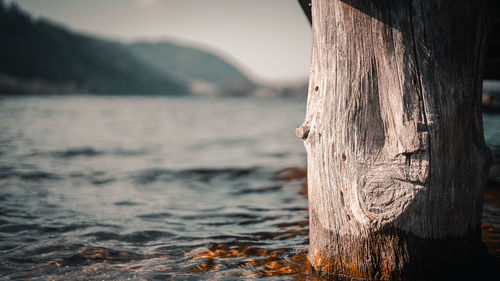 Close-up of wooden post in sea against mountains