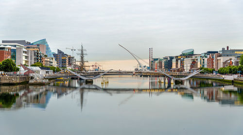 Sailboats moored on river by buildings against sky in city