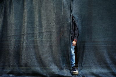 Low section of man hiding behind curtain