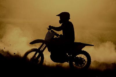 Silhouette man riding motorcycle against sky during sunset