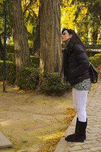 Side view of young woman standing on tree trunk