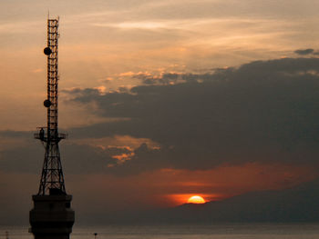 Silhouette tower by sea against sky during sunset