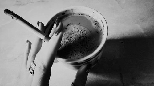 Cropped hand holding cigarette over coffee cup on table