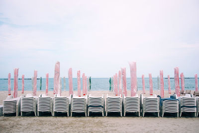 Chairs with parasols at beach against sky