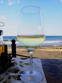 Wine glass on table by sea against sky