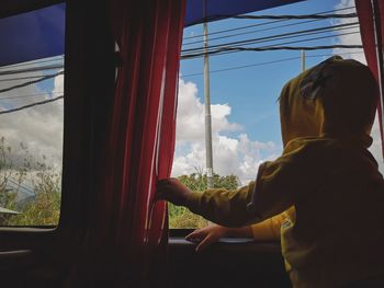 Boy standing by window against sky