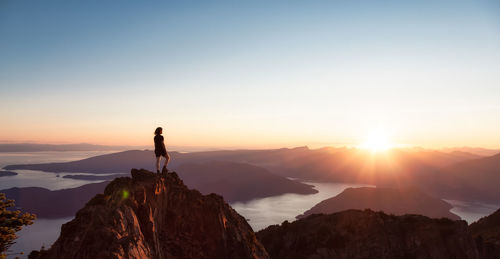 Silhouette woman standing on rock against sky during sunset