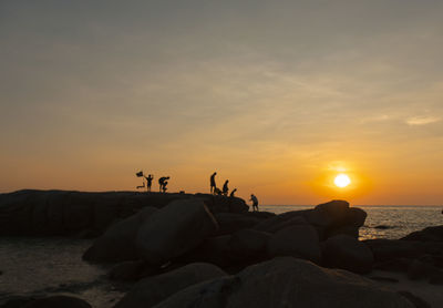 Silhouette rocks on beach against sky during sunset