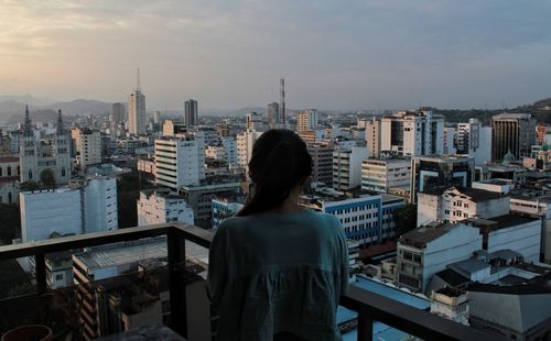 Rear view of woman standing at balcony against cityscape