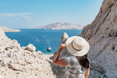 Rear view of woman in summer clothes and sun hat looking at spectacular view and sea coastline.