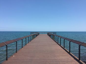 Boardwalk leading to sea against clear sky