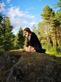 Young woman sitting on rock against sky