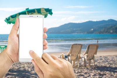 Cropped hands of woman using mobile phone at beach against sky