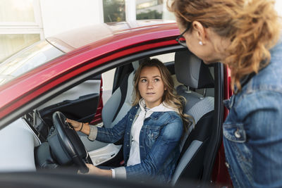 Daughter looking at mother while learning car to drive during vacations