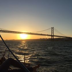 Suspension bridge over sea against clear sky during sunset