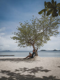 Man sitting on shore at beach against sky